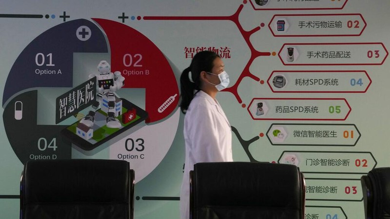 Chen Xiaofang, a nurse at the department of cardiovascular medicine the Guangdong Second Provincial General Hospital, stands next to a robot that delivers medicine in Guangzhou, in southern China's Guangdong province, Sunday, Sept. 26, 2021. The hospital in southern China's Guangdong Province is using 5G and IoT technologies to collect, transmit and monitor more data in real time, allowing healthcare workers to provide better medical service for patients. (AP Photo/Ng Han Guan)