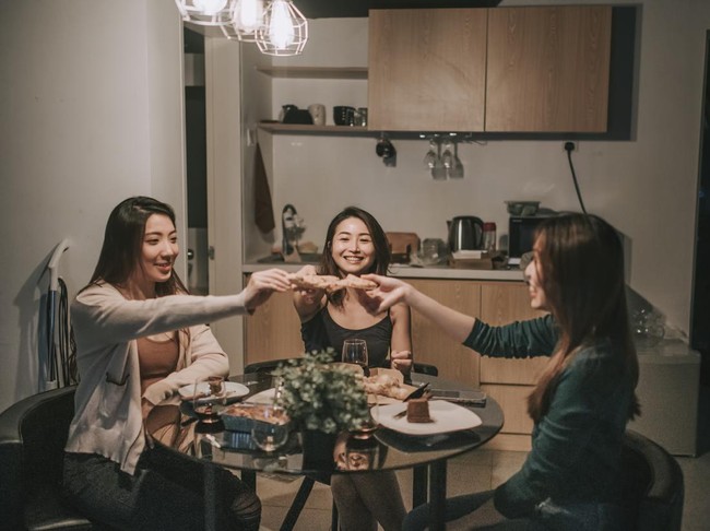 a group of asian chinese female friends having social gathering in apartment eating pizza in dining room at night