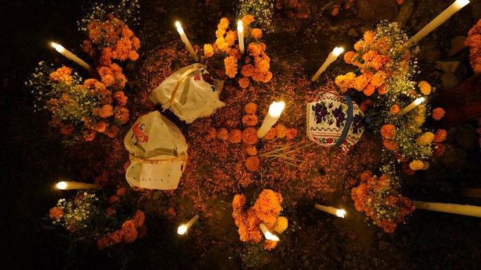 Flowers, food offerings and candles adorn a tomb as relatives spend the night next to the tomb of their loved one during Day of the Dead festivities at the the Arocutin cemetery in Michoacan state, Mexico, Monday, Nov. 1, 2021. In a tradition that coincides with All Saints Day and All Souls Day, families decorate the graves of departed relatives with flowers and candles, and spend the night in the cemetery, eating and drinking as they keep company with their deceased loved ones. (AP Photo/Eduardo Verdugo)