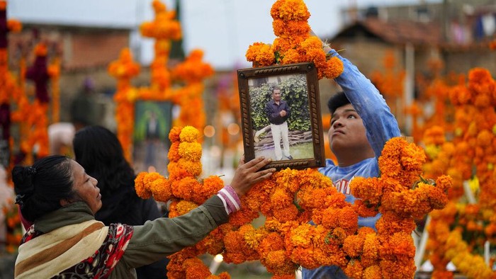 Flowers, food offerings and candles adorn a tomb as relatives spend the night next to the tomb of their loved one during Day of the Dead festivities at the the Arocutin cemetery in Michoacan state, Mexico, Monday, Nov. 1, 2021. In a tradition that coincides with All Saints Day and All Souls Day, families decorate the graves of departed relatives with flowers and candles, and spend the night in the cemetery, eating and drinking as they keep company with their deceased loved ones. (AP Photo/Eduardo Verdugo)