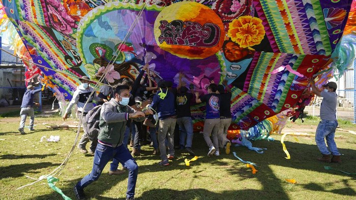 Layang-layang Raksasa Meriahkan Hari Kematian di Guatemala A man helps lift a giant kite to be displayed on All Saints Day as part of Day of the Dead celebrations in Santiago Sacatepequez, Guatemala, Monday, Nov. 1, 2021. For the second year the celebration has been reduced amid some restrictions to help curb the spread of the COVID-19. (AP Photo/Moises Castillo)