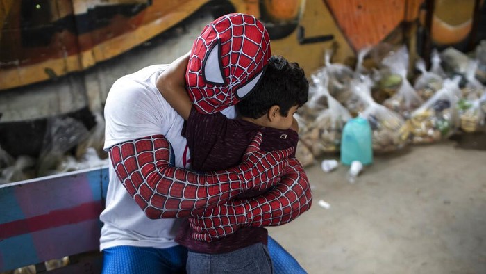 A volunteer dressed as Spiderman embraces a child in the Jardim Gramacho favela of Rio de Janeiro, Brazil, Saturday, Oct. 30, 2021, during a food kit delivery donated by the non-governmental organization 