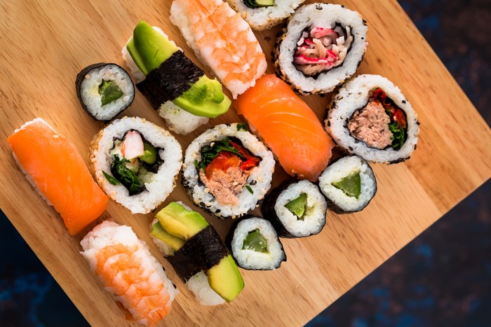 Close up macro color image depicting a delicious arrangement of fresh traditional Japanese sushi rolls topped with smoked salmon, prawn and avocado.
