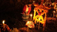 Seorang perempuan menyalakan lilin di sebelah makam orang yang dicintainya pada 1 November 2021. (Eduardo Ferdugo/AP)