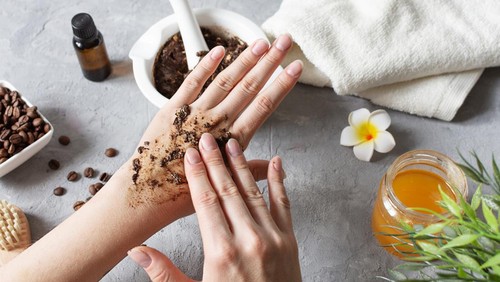 Woman hands making peeling with homemade body scrub made with ground coffee, honey and oatmeal over gray concrete table. Self-care at home, eco homemade cosmetic for spa and skin care.