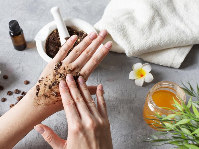 Woman hands making peeling with homemade body scrub made with ground coffee, honey and oatmeal over gray concrete table. Self-care at home, eco homemade cosmetic for spa and skin care.