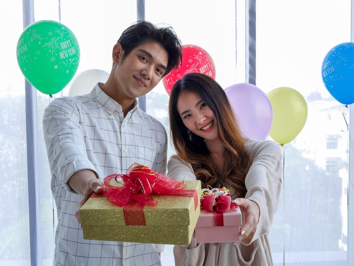 Ilustrasi ulang tahun pacar Beautiful Girl Surprise Her Boyfriend With Gift Celebrating Anniversary While He Is Sitting on the Sofa in the Living Room. Romantic Surprise for Husband Boyfriend, Happy Birthday Concept