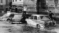 Banjir yang merendam jalan di kawasan Florence pada tahun 1966 ini membuat seorang warga nekat berjalan di atas mobil agar tak kebasahan saat beraktivitas di kala banjir. Keystone/Getty Images.