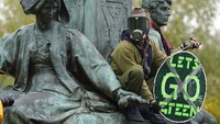 Seorang aktivis memanjat patung publik di pusat kota Glasgow, (5/11/2021).  Tanganya memegang sebuah pesan tertulis Lets Go Green.  (Andrew Milligan/PA via AP)