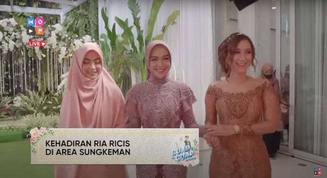 Usai pemasangan bleketepe, ibunda dan paman Ria Ricis pun masuk ke dalam geduung. Tak lama kemudian Ria Ricis masuk ke tempat acara siraman. Ria tampil cantik dalam balutan busana berwarna serba dusty pink. Foto: YouTube/MOP Channel