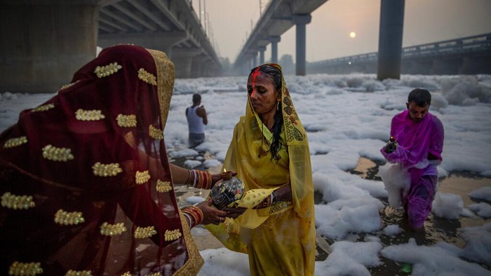 Indian Hindu devotees perform rituals in Yamuna river, covered by chemical foam caused due to industrial and domestic pollution, during Chhath Puja festival in New Delhi, India, Wednesday, Nov. 10, 2021. A vast stretch of one of India's most sacred rivers, the Yamuna, is covered with toxic foam, caused partly by high pollutants discharged from industries ringing the capital New Delhi. Still, hundreds of Hindu devotees Wednesday stood knee-deep in its frothy, toxic waters, sometimes even immersing themselves in the river for a holy dip, to mark the festival of Chhath Puja. (AP Photo/Altaf Qadri)