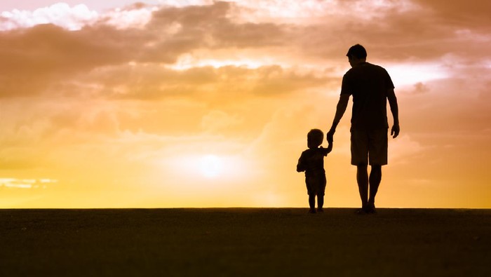 Loving father walking side by side with son holding hands.