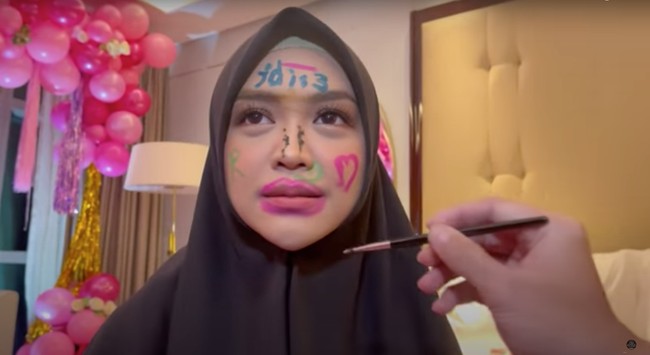 Ria Ricis pun hanya bisa terlihat pasrah wajahnya dicorat-coret oleh para sahabat. Dan begini hasil dari coretan para sahabat di wajah Ricis. Foto: YouTube/Tri Atika