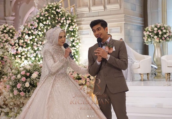 Untuk resepsi Ricis tampil dengan 2 look. Selain gaun berwarna biru, Ricis juga terlihat mengenakan ballgown putih berhias payet. Sedangkan untuk look kedua, Teuku Ryan memilih setelan jas berwarna abu-abu kecoklatan. Penampilannya itu dilengkapi dengan  dasi kupu-kupu. Foto: Instagram/@officialmnctv