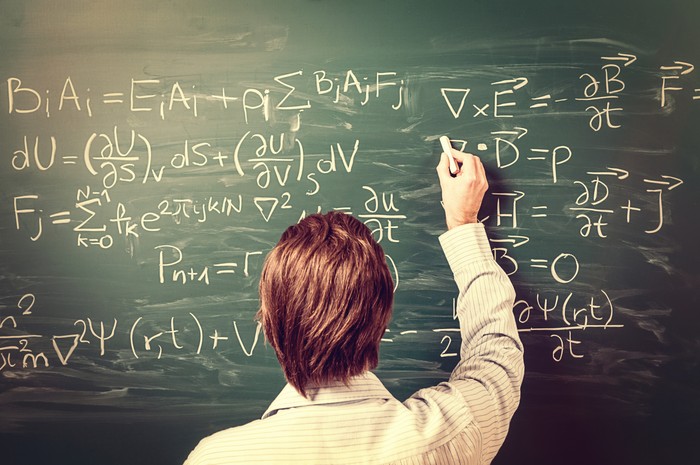 Ilustrasi Guru Matematika Newtons Equations. Rear view, close-up on young man standing back against green chalkboard. He explains, solves physics tasks, retro style. Processing for retro bleached look, slight vignette added.