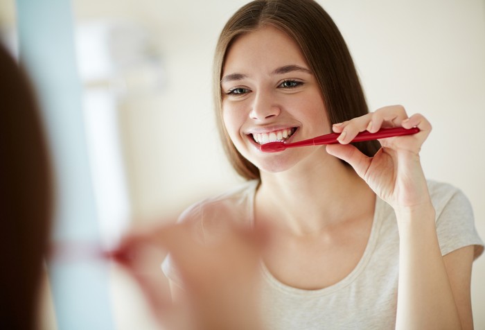 Yooung woman brushing her teeth at mirror