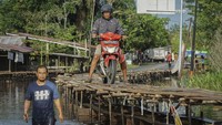 Pengendara sepeda motor melintasi jembatan kayu darurat di atas Jalan Trans Kalimantan Sintang-Putussibau yang terendam banjir di Akcaya, Kabupaten Sintang, Kalimantan Barat.