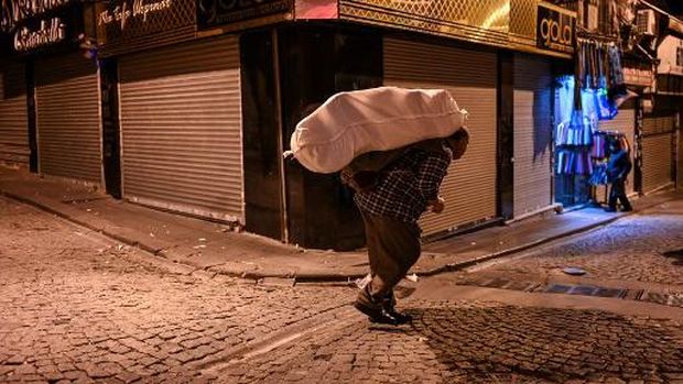 A porter carries belongings on a street early morning, on October 28, 2021 near Grand bazaar in Istanbul. - Just blocks from Istanbul's Grand Bazaar, porter Bayram Yildiz waits his turn in a dark alley to heave a huge bale on his back nearly double his bodyweight. A few others linger beside him, picking up textiles from a lorry and lugging them to local shops before sunrise, their heads bowed and their knees bent.