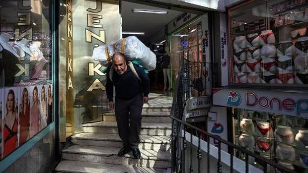 A porter carries belongings on a street early morning, on October 28, 2021 near Grand bazaar in Istanbul. - Just blocks from Istanbul's Grand Bazaar, porter Bayram Yildiz waits his turn in a dark alley to heave a huge bale on his back nearly double his bodyweight. A few others linger beside him, picking up textiles from a lorry and lugging them to local shops before sunrise, their heads bowed and their knees bent.