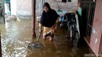 Seorang warga membersihkan sampah yang ikut terbawa air banjir.