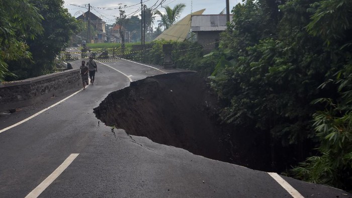 Warga melintas di dekat jalan ambles di Desa Pejeng, Gianyar, Bali, Selasa (16/11/2021). Amblesnya jalan raya yang merupakan jalur akses menuju Kota Gianyar itu disebabkan kelabilan tanah setelah terjadi hujan deras pada Senin (15/11/2021) dan tidak ada korban dalam peristiwa itu. ANTARA FOTO/Nyoman Hendra Wibowo/rwa.