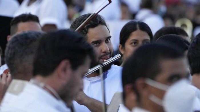 Nicolas Maduro Guerra, center, son of Venezuelan President Nicolas Maduro, takes part in an attempt to try and break a Guinness World Record in Caracas, Venezuela, Saturday, Nov. 13, 2021. The musicians, all connected with the country network of youth orchestras, played at a military base under the watchful eyes of hundreds of independent supervisors tasked with verifying that more than 8,097 instruments are played at the same time. (AP Photo/Ariana Cubillos)
