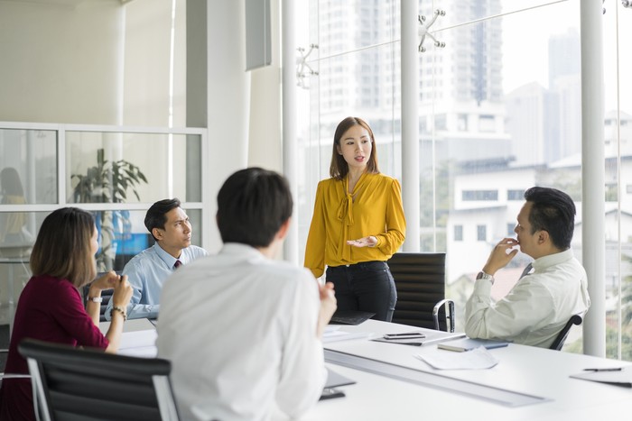 Confident businesswoman giving presentation in board room. Professionals are in meeting at conference table. They are sharing ideas in office.