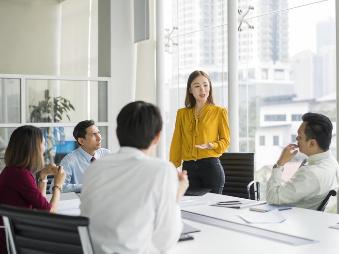 ilustrasi wanita karier Confident businesswoman giving presentation in board room. Professionals are in meeting at conference table. They are sharing ideas in office.