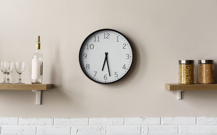 Round wall clock between wooden kitchen shelves showing time