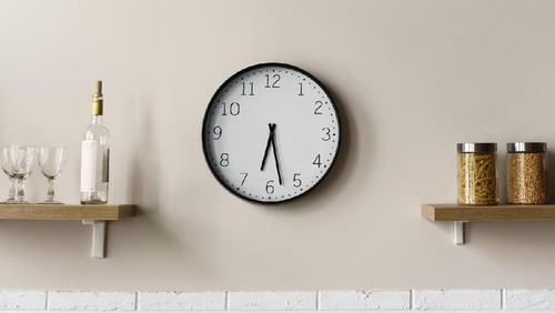 Round wall clock between wooden kitchen shelves showing time