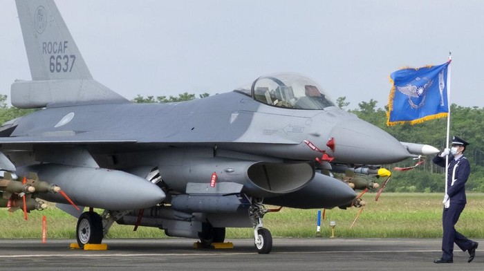 A Taiwanese Air Force flag bearer passes by one of the newly commissioned upgraded F-16V fighter jets at Air Force base in Chiayi in southwestern Taiwan Thursday, Nov. 18, 2021. Taiwan has deployed the most advanced version of the F-16 fighter jet in its Air Force, as the island steps up its defense capabilities in the face of continuing threats from China. (AP Photo/Johnson Lai)