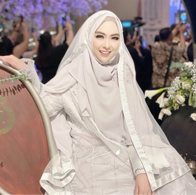 Dalam rangkaian acara pernikahan Ria Ricis, dr. Shindy memakai dress dari Irna Perle Official, karya perancang busana Irna Mutiara. Shindy memakai veil wedding, hijab syari dan dress dengan layering look warna silver. Penampilannya langsung mendapatkan pujian dari warganet. Cantiik banget ka MasyaAllah 😍,puji akun @adindaamiraa. Barbie hidup, puji akun @hanaa_nhha12. Masya Allah cantiknya dokter shindy❤️ @dr.shindyputri_, ucap @fitrh_22. Foto: Dok. Instagram @dr.shindyputri_.