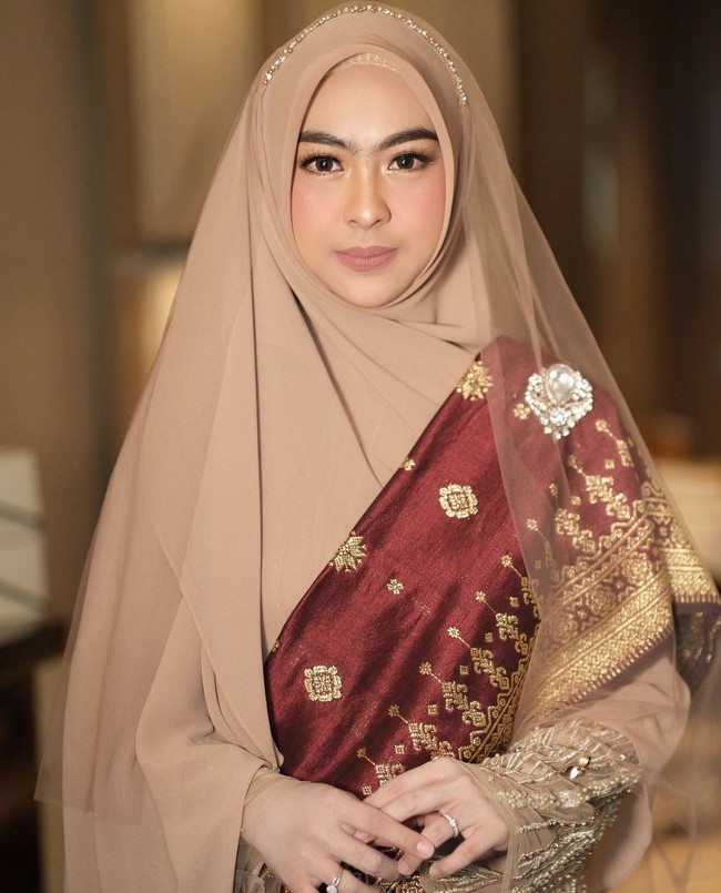 Sosok Shindy mencuri perhatian warganet ketika menghadiri acara pernikahan Ria Ricis. Ia mengenakan kebaya warna cokelat dari perancang busana Anji Asmara, dipadu dengan kain selendang songket merah. Shindy memakai hijab syari mocca yang membuat penampilannya semakin memesona. Foto: Dok. Instagram @dr.shindyputri_.