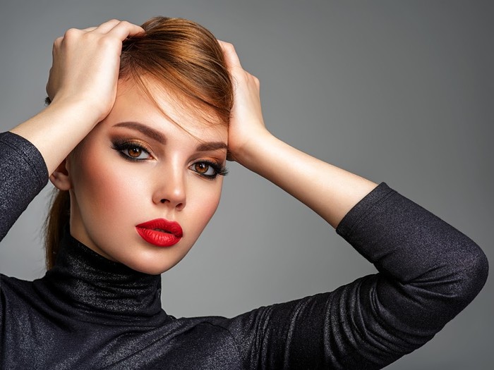 Beautiful girl with red lips and short hair. Pretty face of an young sensual woman. Closeup portrait of a model with bright makeup on a face. Attractive female posing at studio  in black closes.