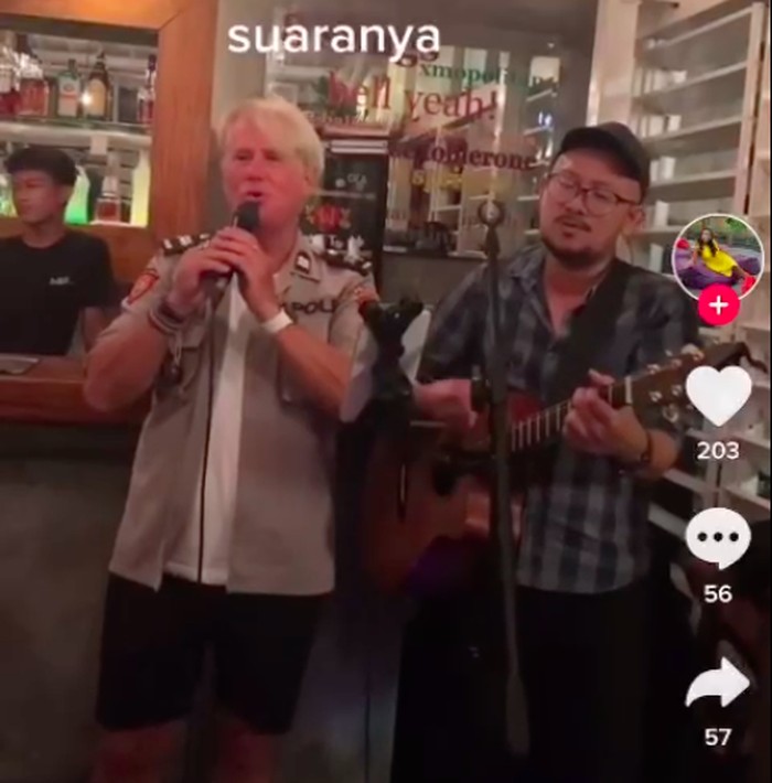 Seorang WNA di Bali bernyanyi di sebuah kafe dengan mengenakan baju mirip instansi Polri viral di medsos. Polisi turun tangan mengusut kasus tersebut. (Screenshot video viral)