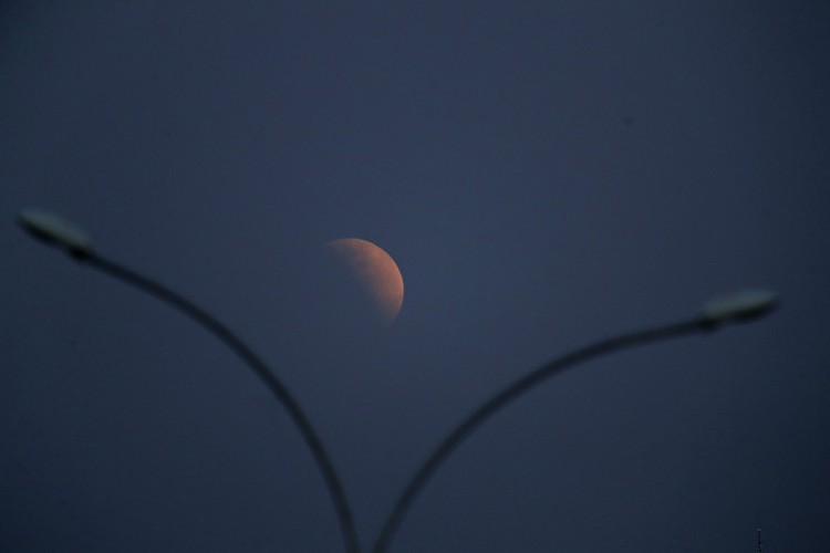 I this Tuesday, July 16, 2019 photo, men stand below street lights as the moon rises during a partial lunar eclipse in Buenos Aires, Argentina. (AP Photo/Natacha Pisarenko)