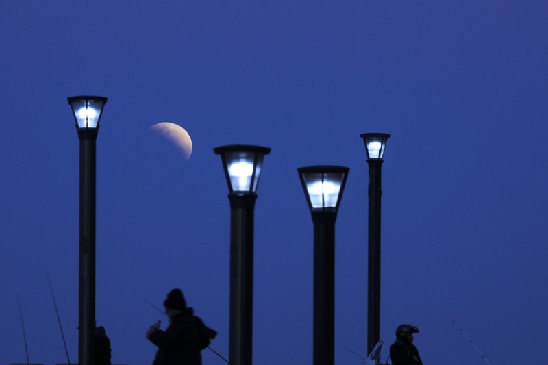 I this Tuesday, July 16, 2019 photo, men stand below street lights as the moon rises during a partial lunar eclipse in Buenos Aires, Argentina. (AP Photo/Natacha Pisarenko)