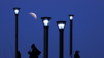 Seorang pria berdiri di bawah lampu jalan ketika Bulan terbit saat gerhana Bulan parsial di Buenos Aires, Argentina, Selasa, 16 Juli 2019. Foto: AP/Natacha Pisarenko