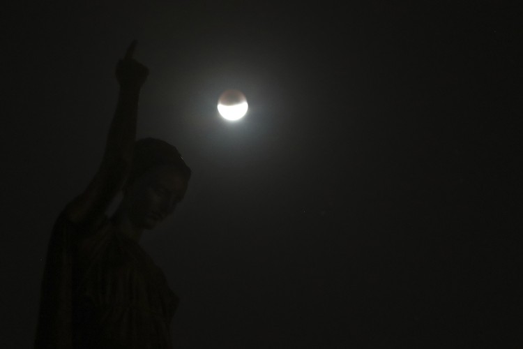 I this Tuesday, July 16, 2019 photo, men stand below street lights as the moon rises during a partial lunar eclipse in Buenos Aires, Argentina. (AP Photo/Natacha Pisarenko)