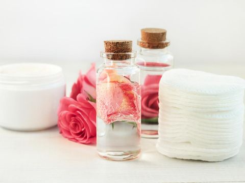 Glass bottle with attar bubbles and rose petals, cotton pads. Healing homemade skincare moisture toni
