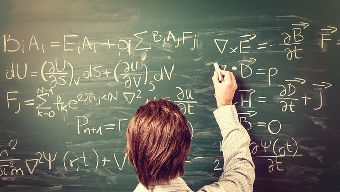 Newtons Equations. Rear view, close-up on young man standing back against green chalkboard. He explains, solves physics tasks, retro style. Processing for retro bleached look, slight vignette added.