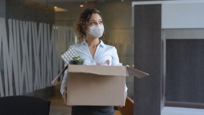Female worker wearing a facemask at the office while holding a box with her belongings after being fired from her job during the COVID-19 pandemic