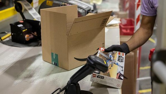 Pekerja mengepak barang saat memenuhi pesanan di gudang Amazon di Brieselang, Jerman, Minggu (22/11/2021).
