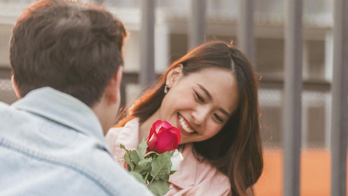 young happy couple love and romantic at first date relationship. asian teenage woman surprise and smiling at boyfriend gives red rose flowers at dinner in valentine day. focus on rose flower.