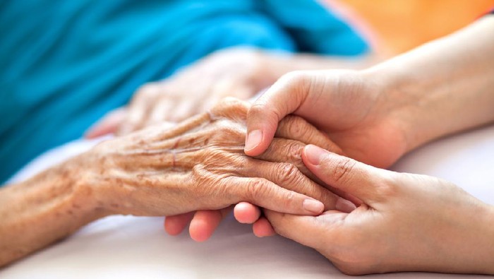 Woman holding senior womans hand on bed