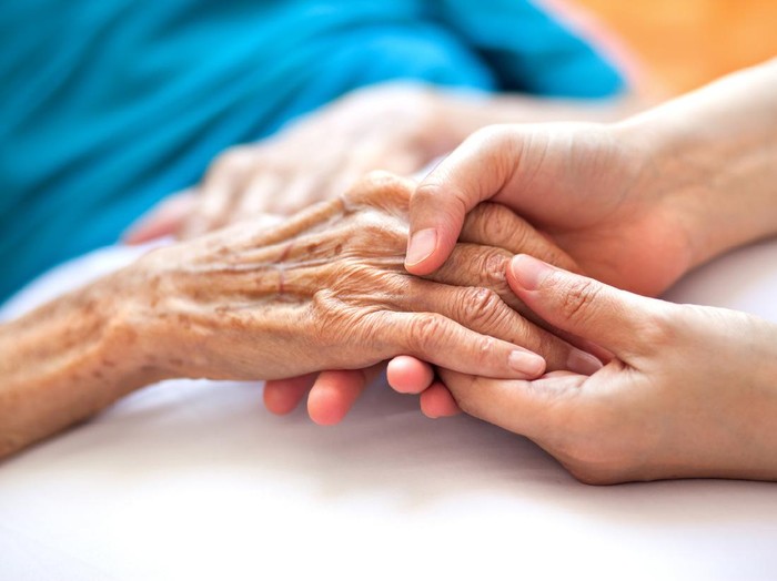 Woman holding senior womans hand on bed