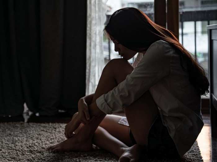 1173052440 Selective focus loneliness young asian woman sitting on bedroom floor near the balcony. Depression sadness breaking up asian teenage girl sitting alone hugging knees closing eyes and thinking.