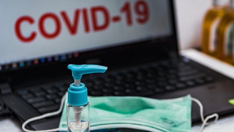 Hand sanitizer bottle and surgical mask on a laptop keyboard that reads COVID-19 on the screen. The concept of preventing office employees from coronavirus disease pandemic.