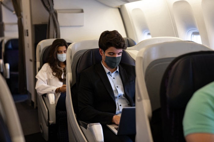 Business man traveling and wearing a facemask on the plane while using his laptopâ COVID-19 pandemic lifestyle concepts