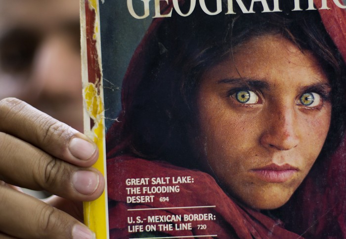 FILE - In this file photo taken on Oct. 26, 2016, Pakistans Inam Khan, owner of a book shop shows a copy of a magazine with the photograph of Afghan refugee woman Sharbat Gulla, from his rare collection in Islamabad, Pakistan. National Geographic’s famed green-eyed “Afghan Girl” has arrived in Italy as part of the West’s evacuation of Afghans following the Taliban takeover of the country, the Italian government said Thursday. The office of Premier Mario Draghi said Italy had organized the evacuation of Sharbat Gulla after she asked to be helped to leave the country. The Italian government will now help to welcome her and get her integrated into life here, the statement said.(AP Photo/B.K. Bangash, File)